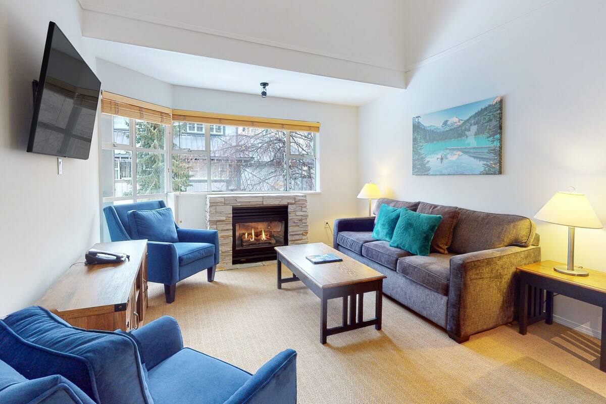 A living room with a fireplace, blue sofas, a coffee table, and a painting on the wall.