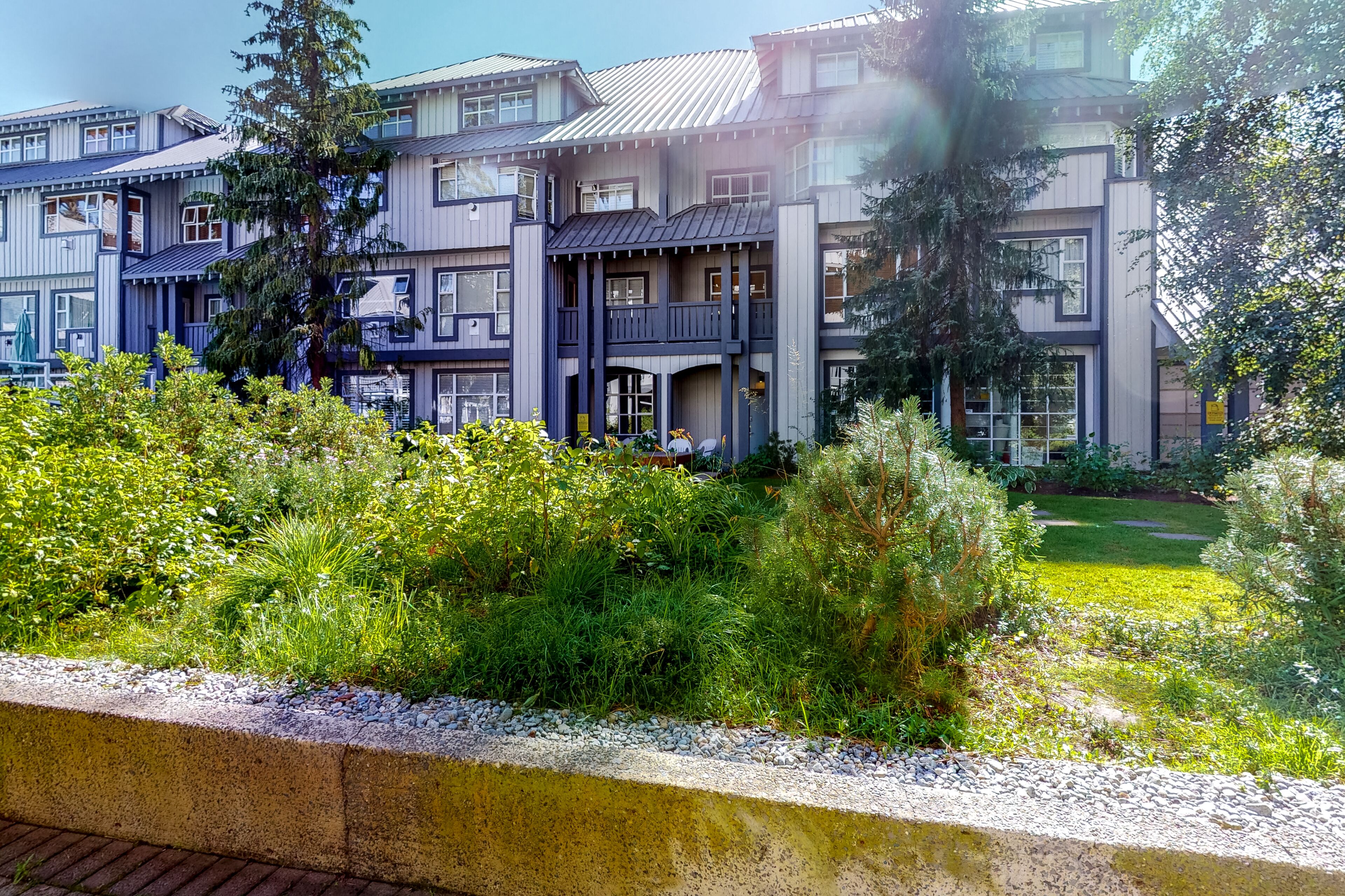A multi-story residential building with balconies, a garden area, and a paved walkway.