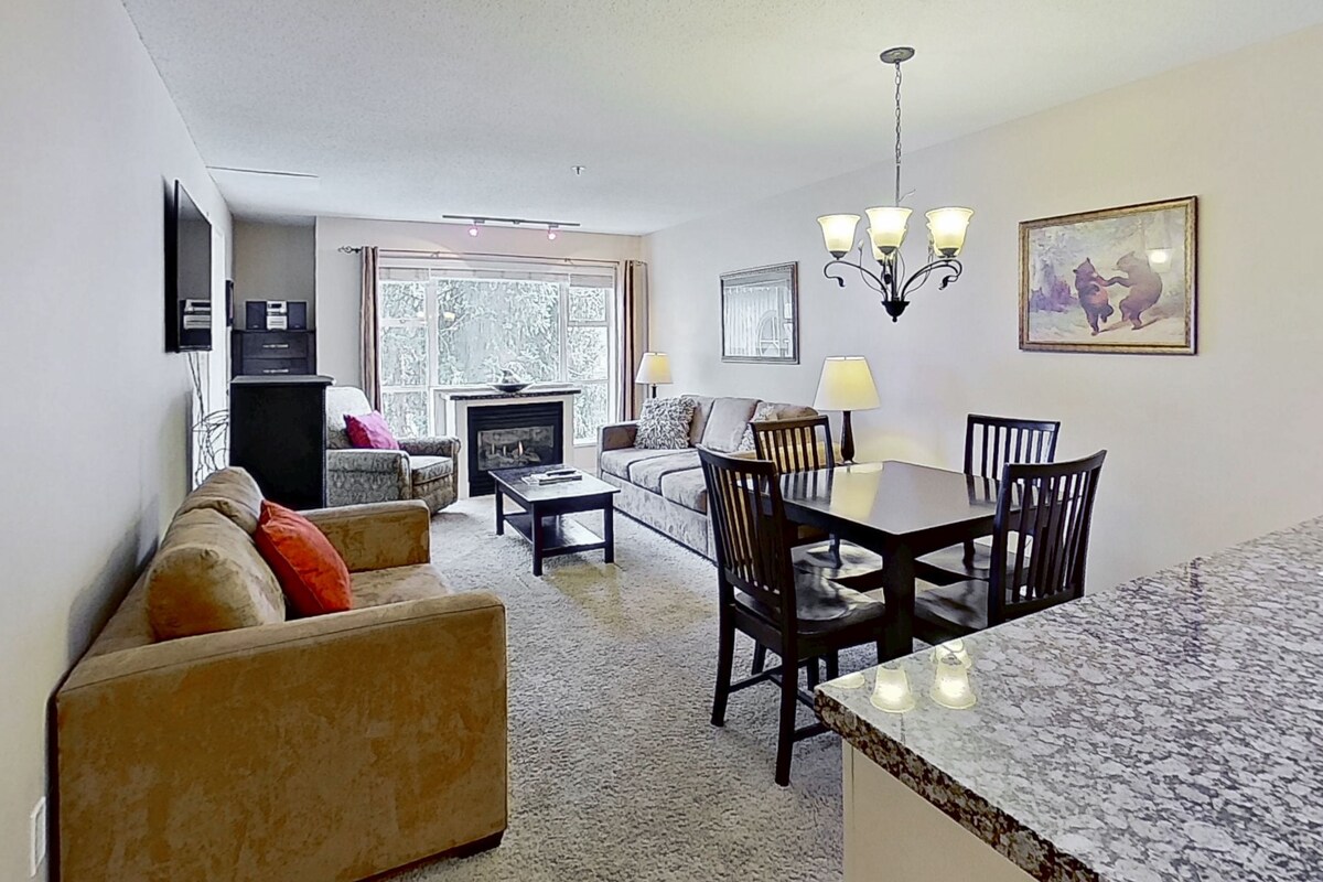 A living room with a sofa, a dining table with chairs, a fireplace, and a chandelier.