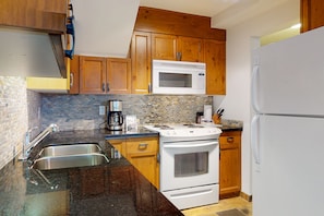 A kitchen with wooden cabinets, a white stove, a microwave, and a refrigerator.