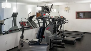 Een sportschool met loopbanden, elliptische trainers en een spiegelwand.