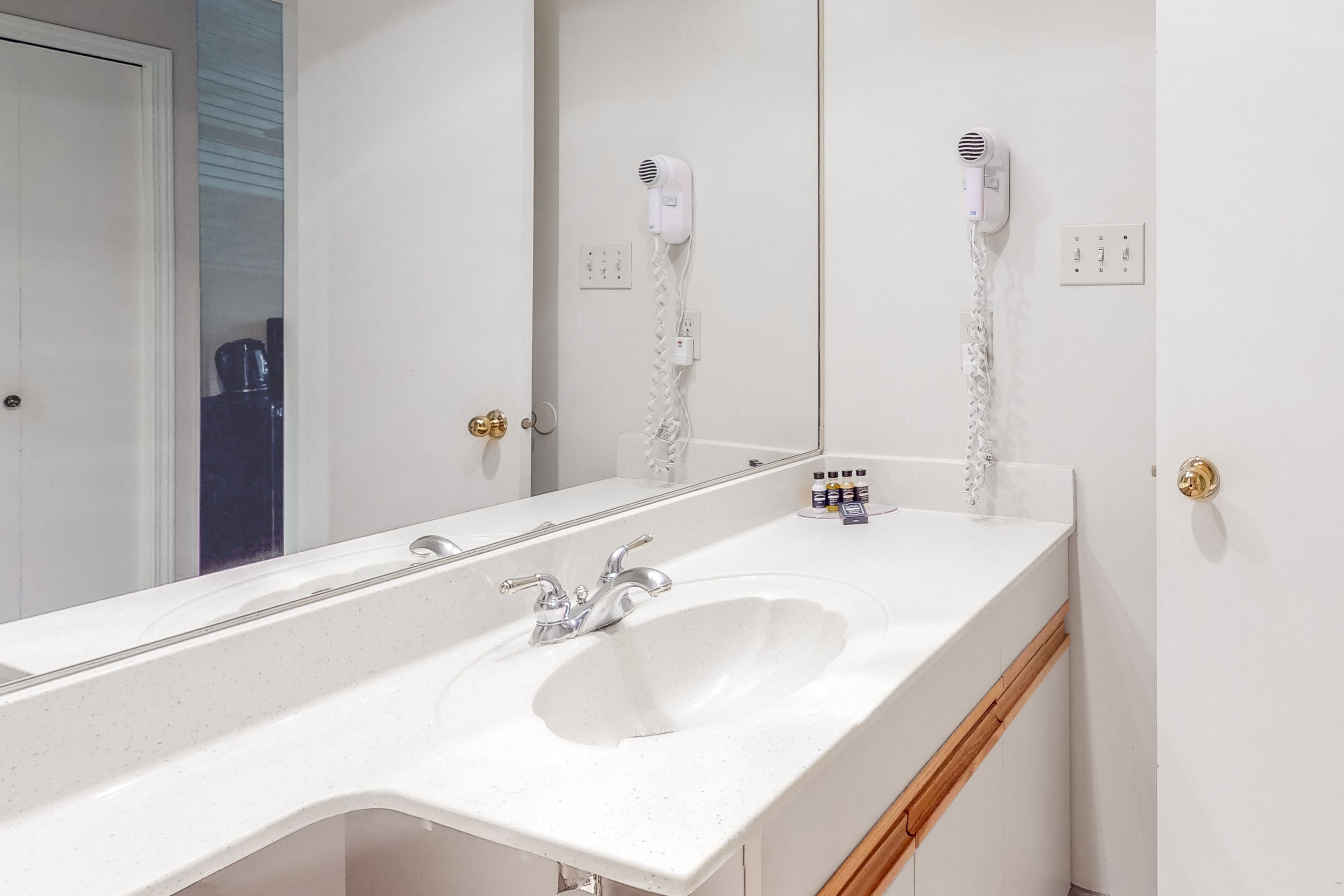 A bathroom with a white sink, a mirror, and two hair dryers mounted on the wall.