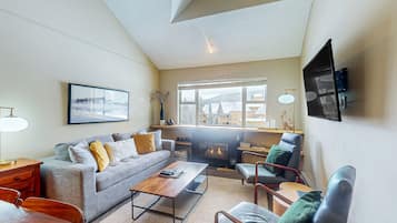 Un salón moderno con chimenea, asientos confortables y un ventanal que ofrece vistas a edificios.