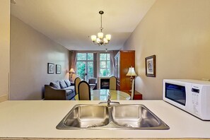Una cocina moderna con un lavamanos doble, un microondas y una zona de comedor con una mesa y sillas de vidrio.