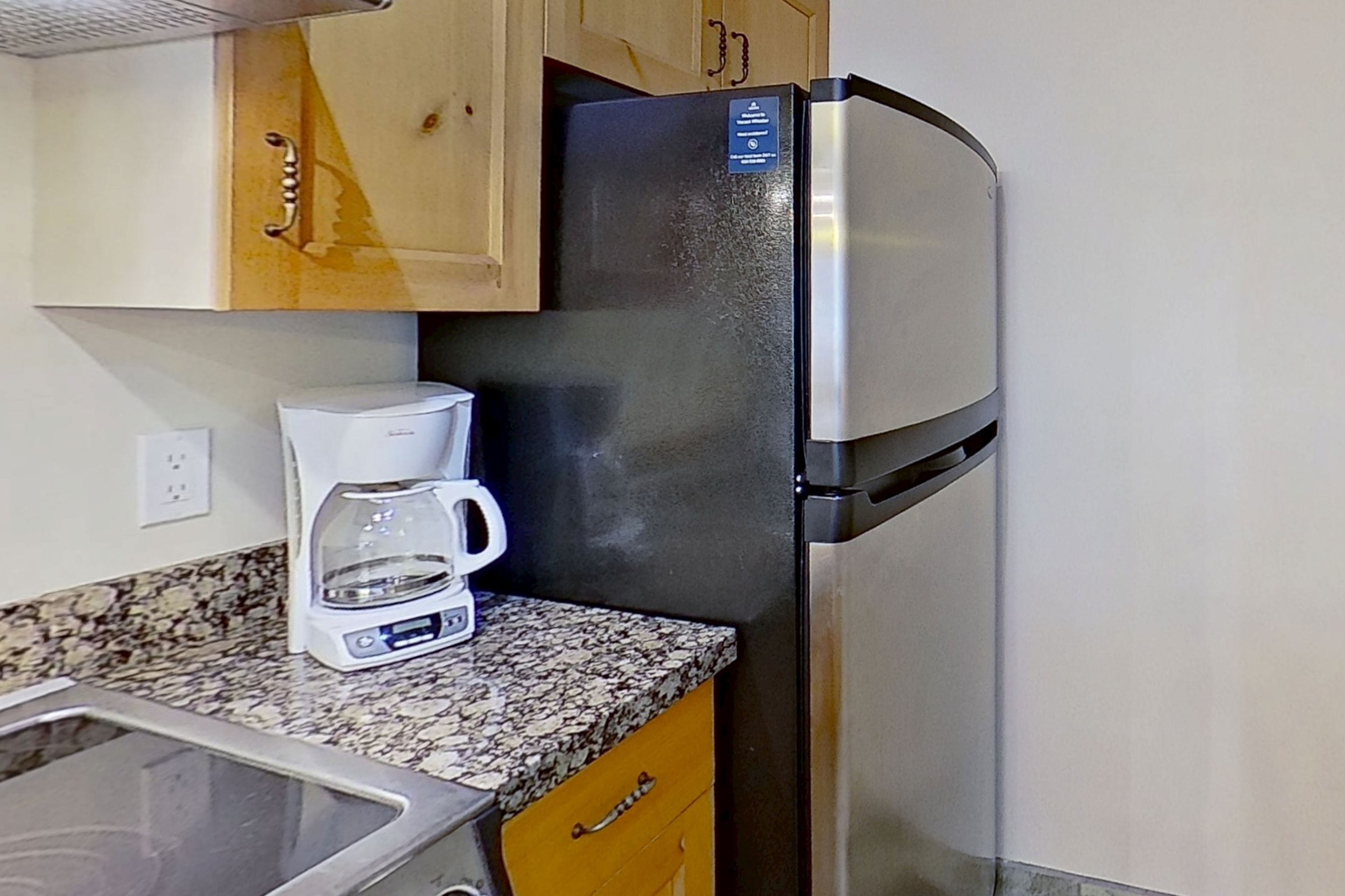 Una cocina con un refrigerador de acero inoxidable, una cafetera y armarios de madera.