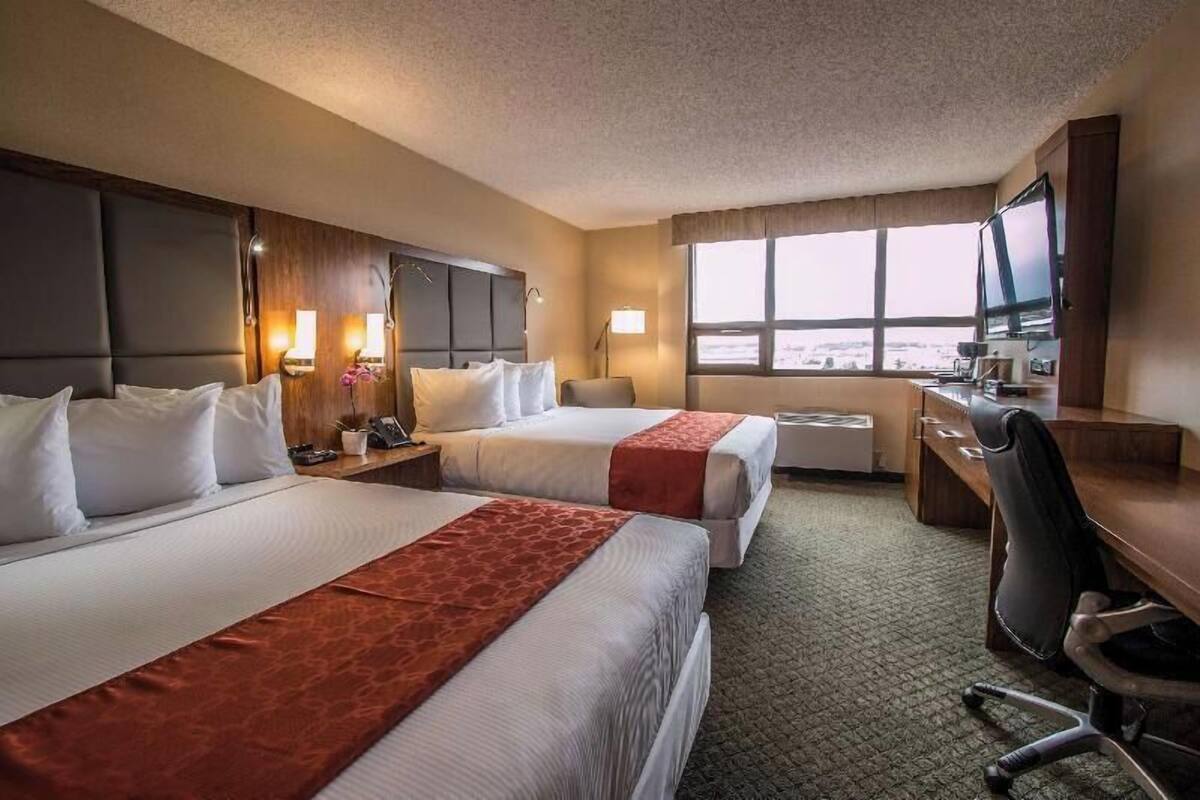 Habitación de hotel con dos camas, un escritorio, una silla, un televisor y una ventana con vistas.