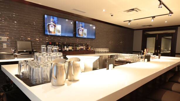 Un bar moderne doté d’un long comptoir, de nombreux verres et d’un téléviseur fixé au mur.