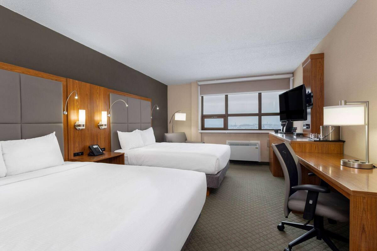 Una habitación de hotel con dos camas, un escritorio, una silla, un televisor y una ventana.