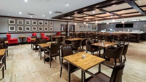 Un restaurant moderne avec des tables et des chaises en bois, un coin bar et des tableaux encadrés aux murs.