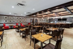 Un restaurante moderno con mesas y sillas de madera, una zona de bar y cuadros en las paredes.