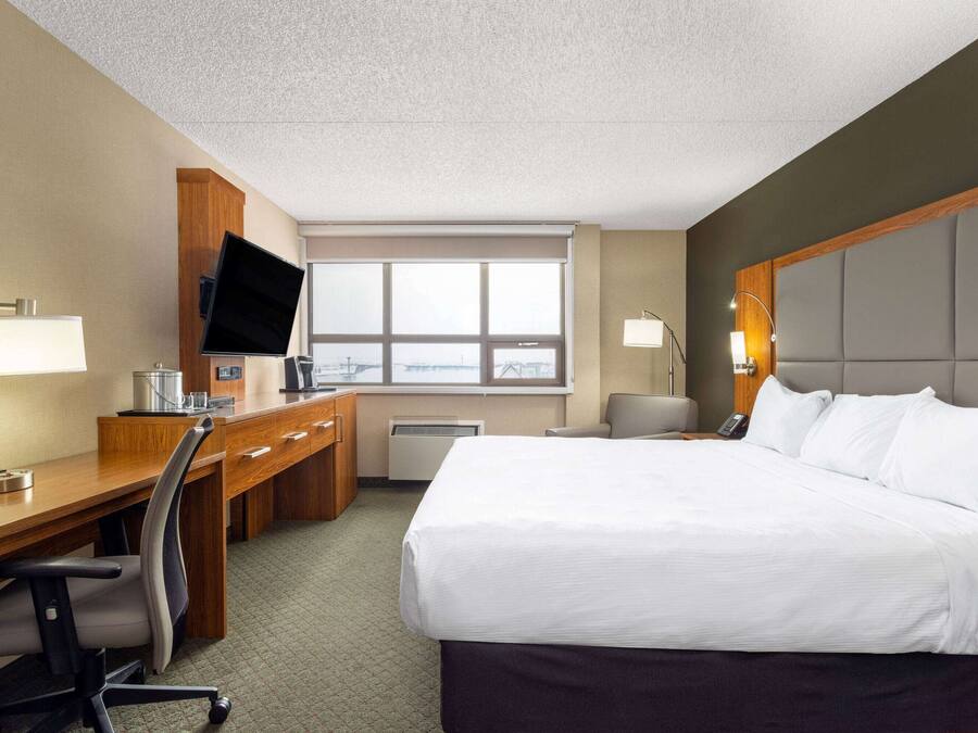 Quarto de hotel com cama, escrivaninha, cadeira, televisão e janela com vista.