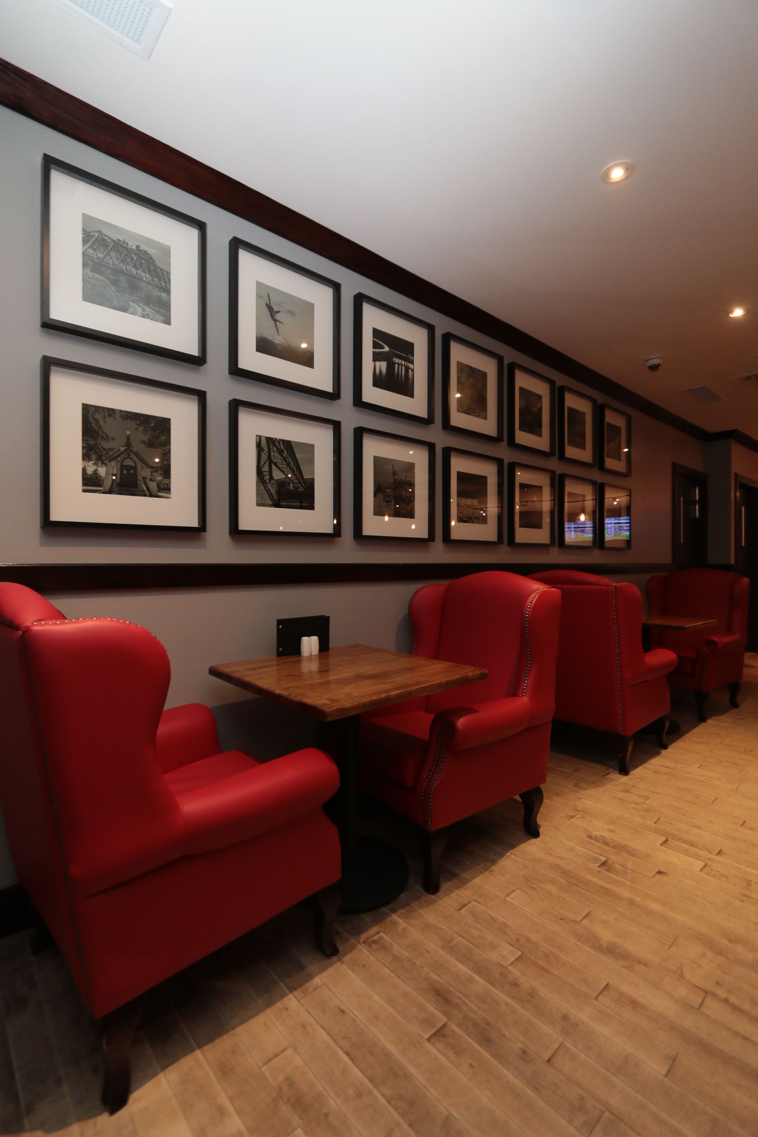 A restaurant interior with red upholstered chairs, a wooden table, and framed pictures on the wall.