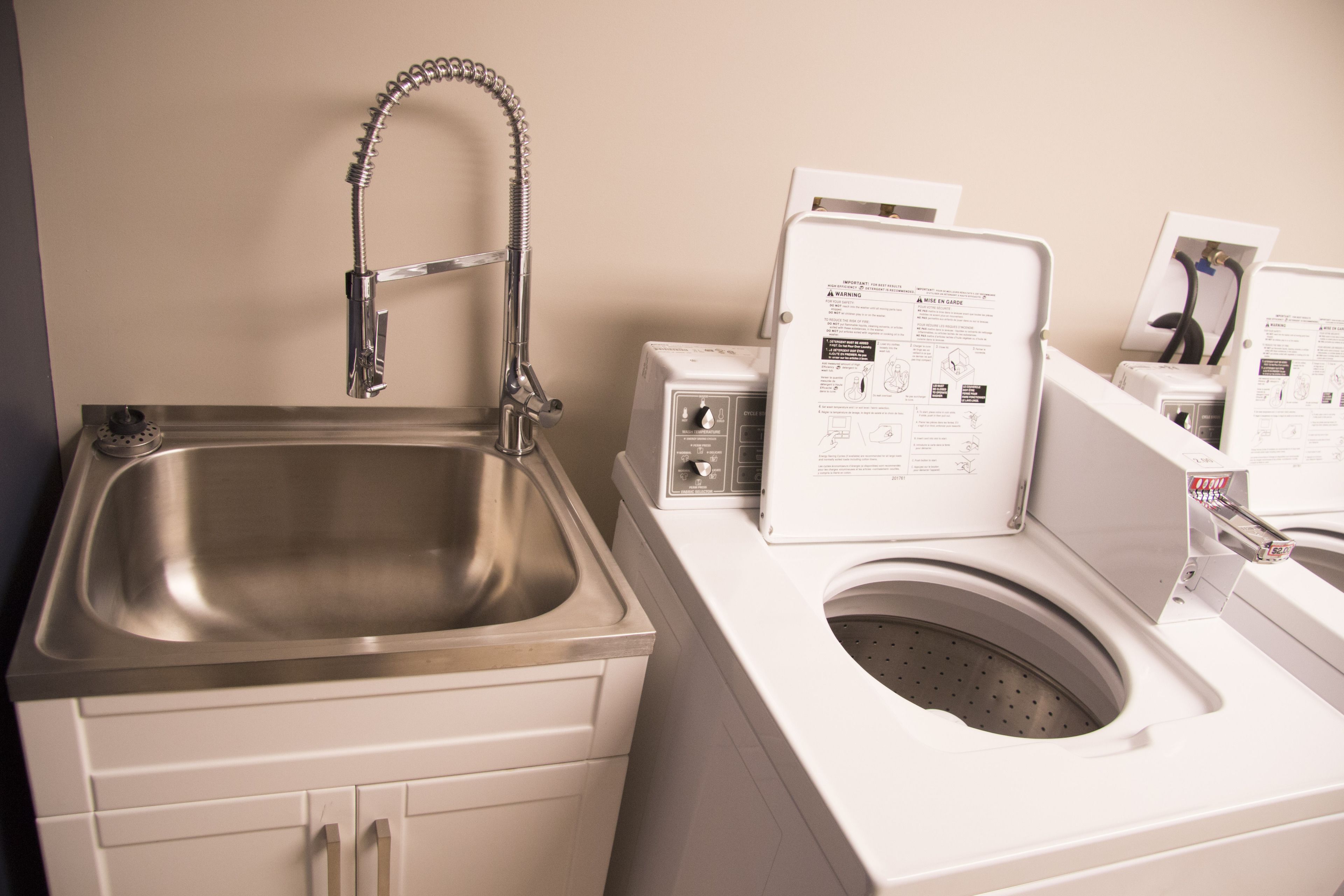 A modern bathroom with a stainless steel sink, a built-in washing machine, and a toilet.