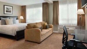 A hotel room with a bed, a sofa, a desk with a chair, and a TV.