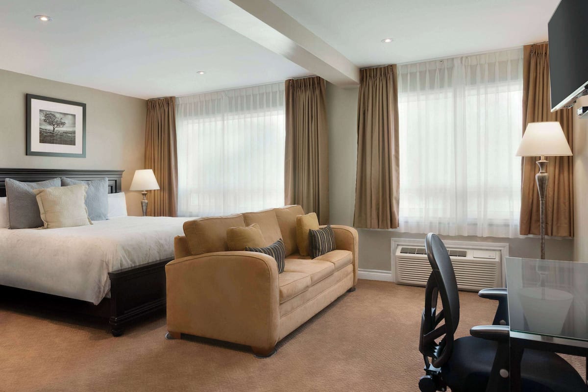 A hotel room with a bed, a sofa, a desk with a chair, and a TV.