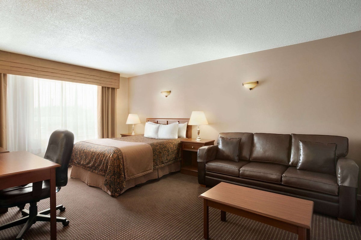A hotel room with a bed, a sofa, a desk, and two lamps.