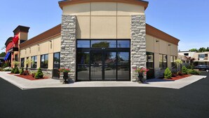 A modern building with a curved roof, large glass entrance, stone pillars, and landscaped areas with shrubs and flowers.