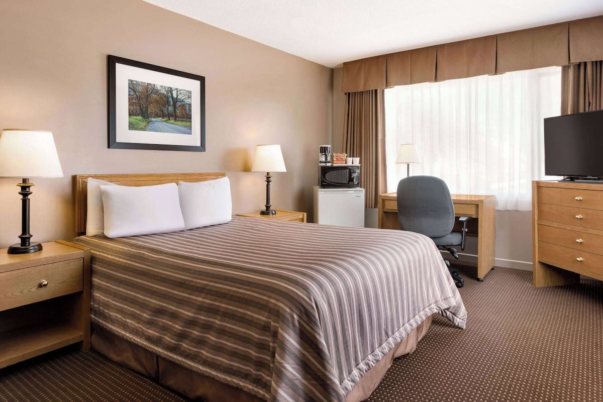 A hotel room with a bed, a desk, a television, and a window with curtains.