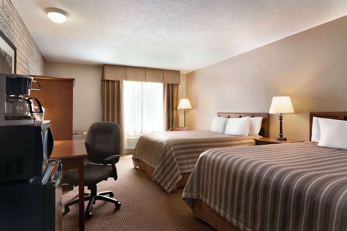 A hotel room with two beds, a desk with a coffee maker, a chair, and a TV.