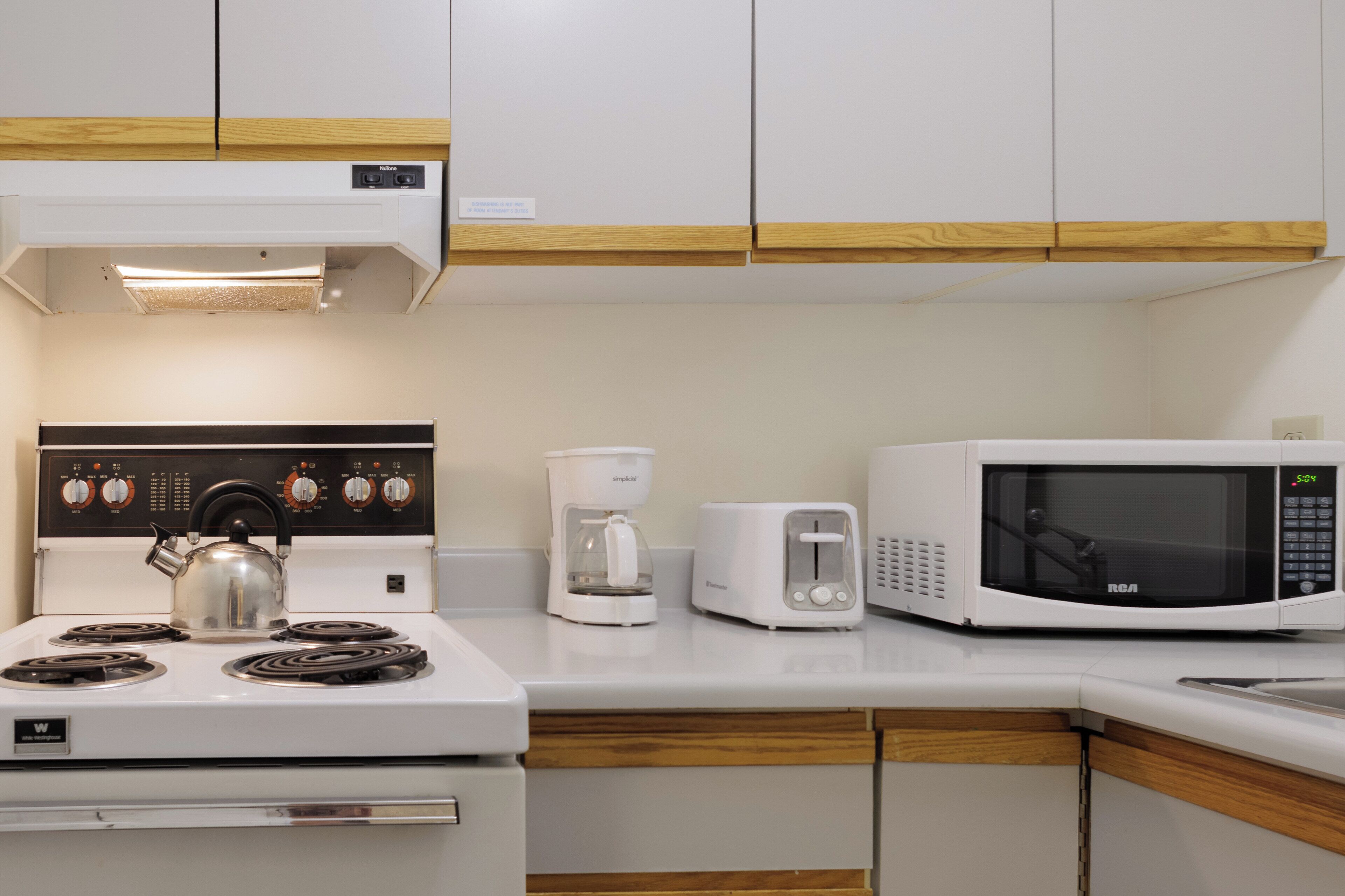 A kitchen with a stove, kettle, coffee maker, and microwave.