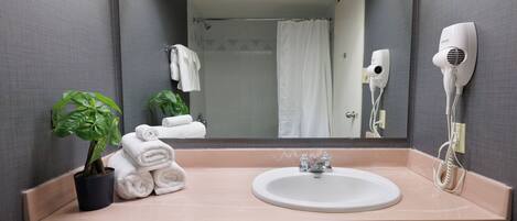 Uma casa de banho com uma pia, um espelho, um porta-toalhas, um secador de cabelo e uma planta em vaso.