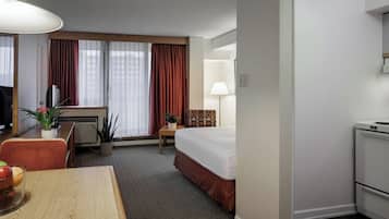A hotel room with a bed, desk, chair, lamp, and a small kitchenette.