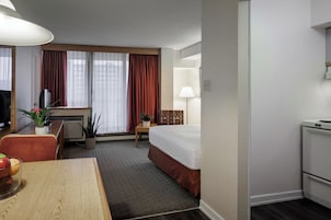 Habitación de hotel con cama, escritorio, silla, lámpara y una pequeña kitchenette.