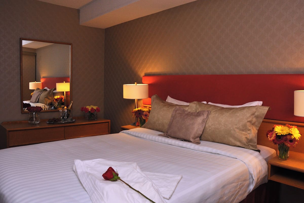 A hotel room with a large bed, two bedside tables with lamps, a dresser, and a mirror.