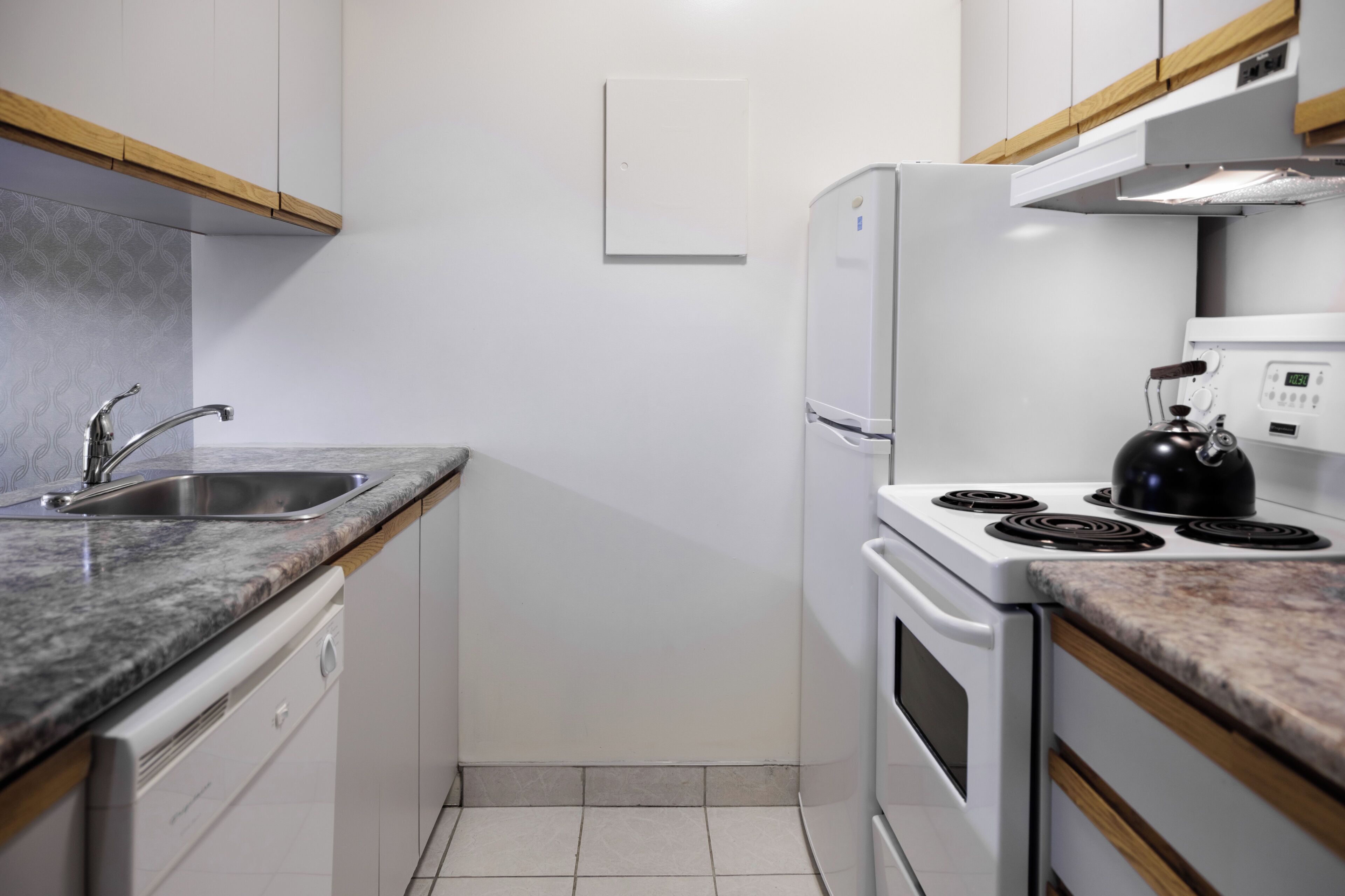 A compact kitchen with a sink, stove, and refrigerator, featuring white cabinetry and a granite countertop.