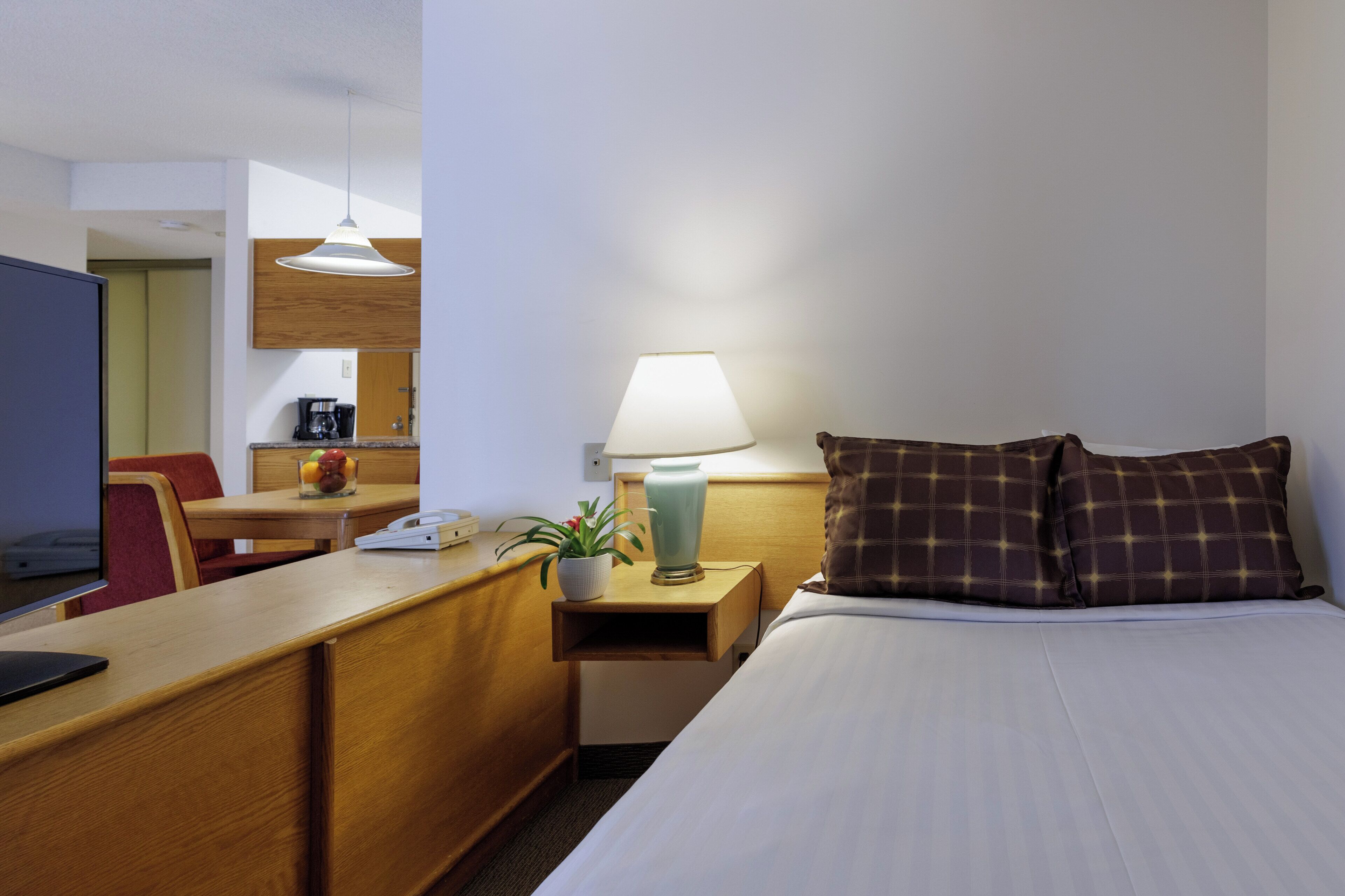 Une chambre d’hôtel comprenant un lit, un bureau, une chaise, une lampe et une petite table agrémentée d’une plante et d’un vase.
