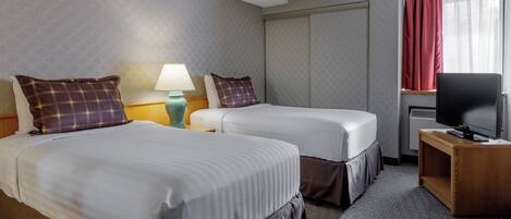 A hotel room with two beds, a television, a lamp, and a window with curtains.