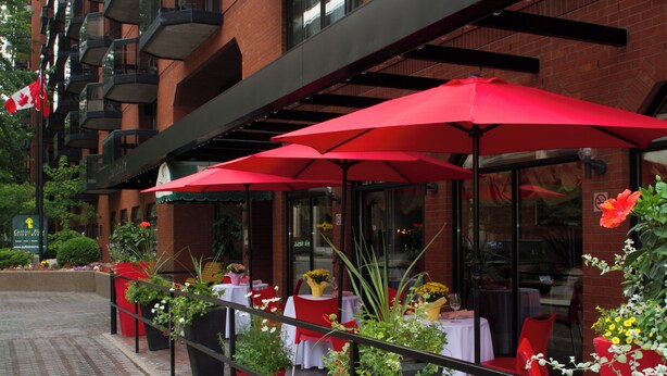 An outdoor dining area with red umbrellas, potted plants, and red chairs. - Cartier Place Suite Hotel (Ottawa)