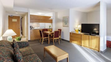 A living room with a sofa, a wooden coffee table, a TV, a dining area with chairs and a table, and a kitchen in the background.