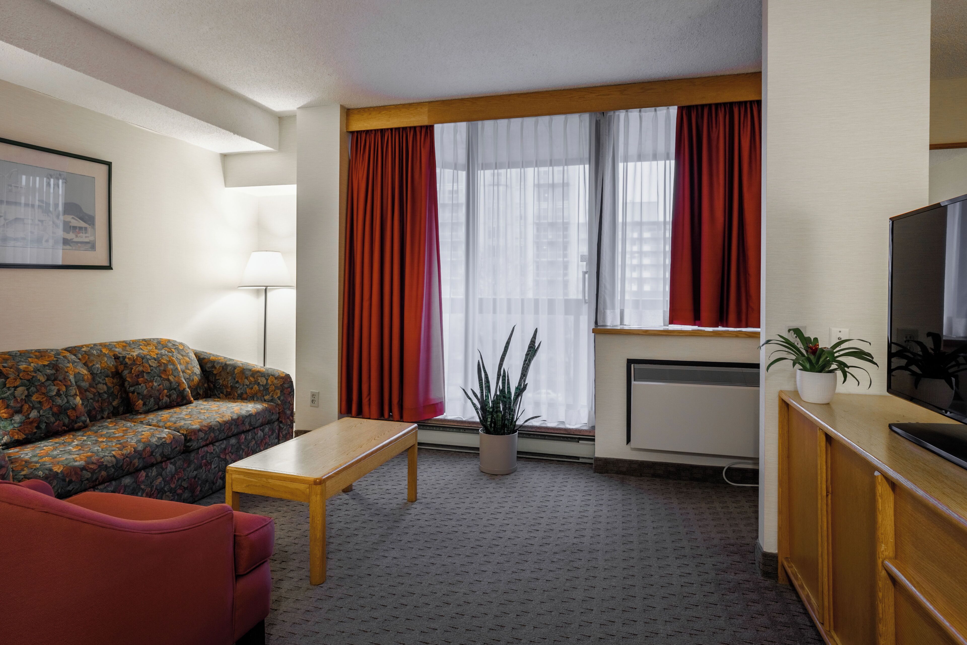 A hotel room with a sofa, a small table, a television, and a window with curtains.
