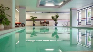 An indoor swimming pool with clear water, surrounded by potted plants, a table with chairs, and a view of the outside through large windows. - Cartier Place Suite Hotel (Ottawa)