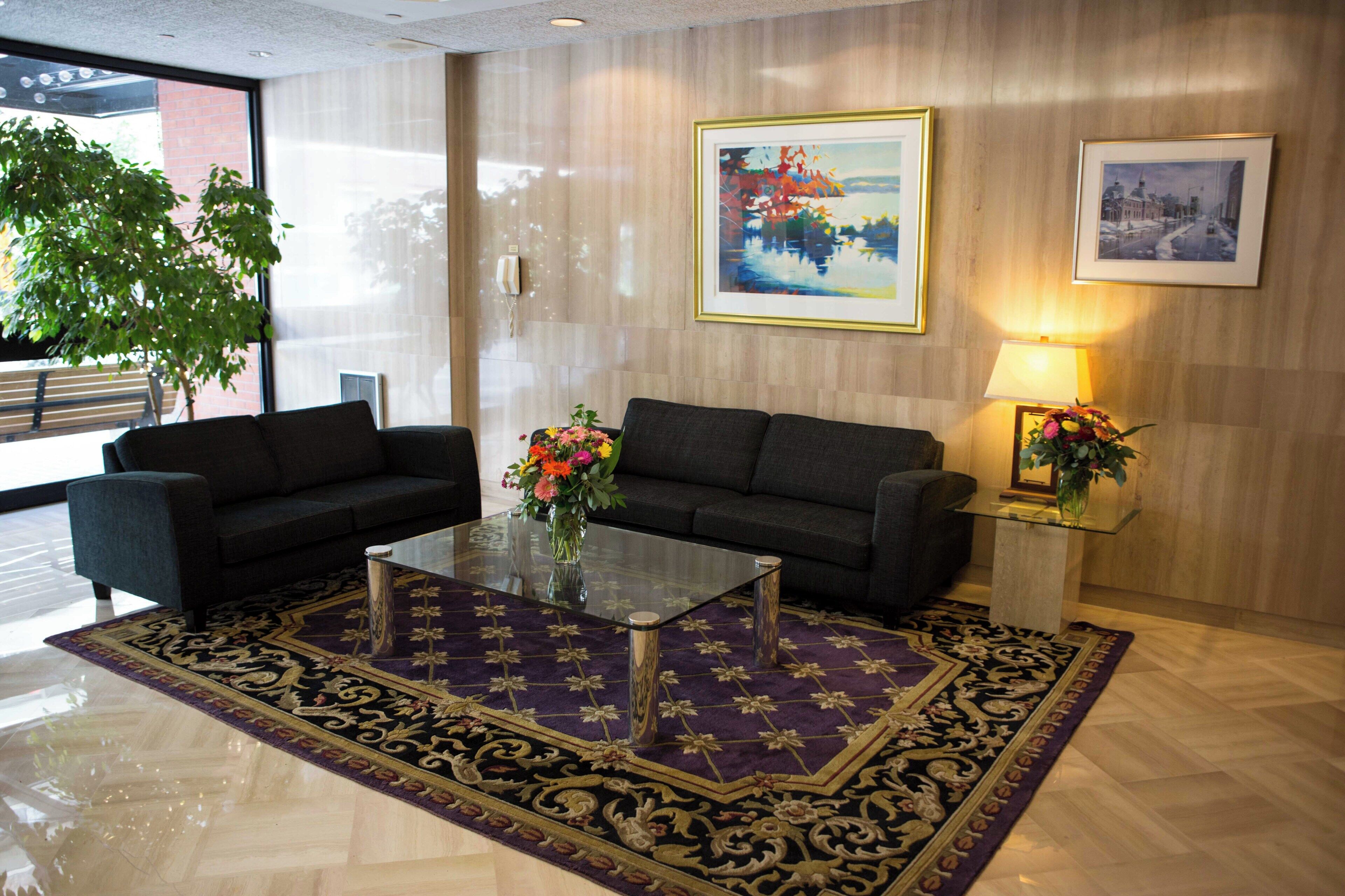Un hall d’entrée moderne avec deux canapés, une table basse en verre, un tapis à motifs et deux tableaux encadrés accrochés au mur.