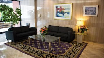 A modern lobby with two sofas, a glass coffee table, a patterned rug, and two framed pictures on the wall.