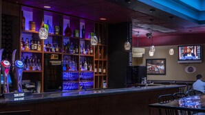 A bar area with shelves of liquor bottles, a television screen, and hanging pendant lights. - Paradise Inn & Conference Centre (Grande Prairie)