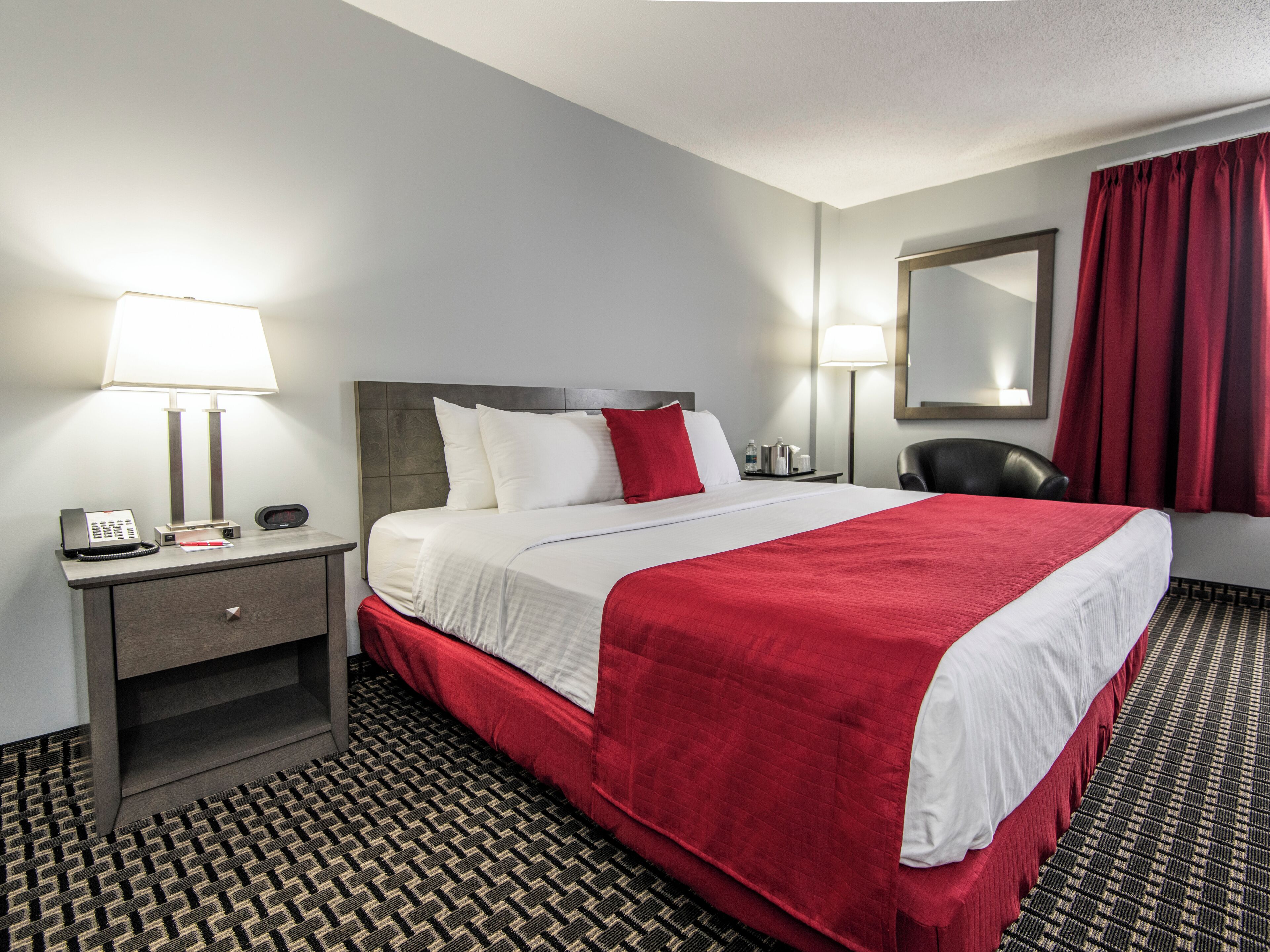 A hotel room with a bed, bedside lamps, a telephone, a chair, and a mirror.