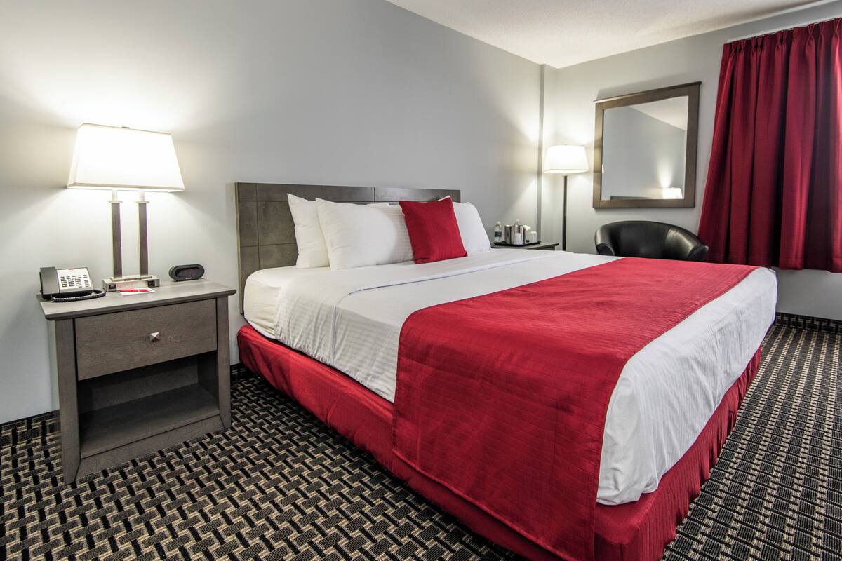 A hotel room with a bed, bedside lamps, a telephone, a chair, and a mirror.