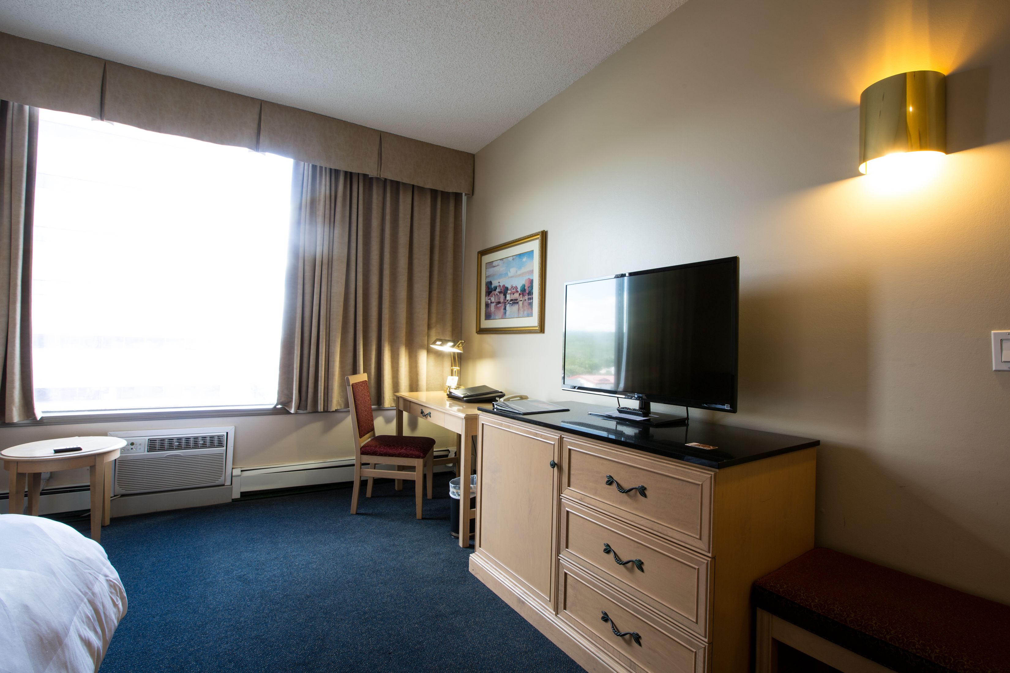 A hotel room with a bed, a desk with a chair, a television, and a window with curtains.