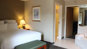 Una habitación de hotel con una cama, una mesita de noche con lámpara, un cuadro en la pared y un baño con bañera y espejo.