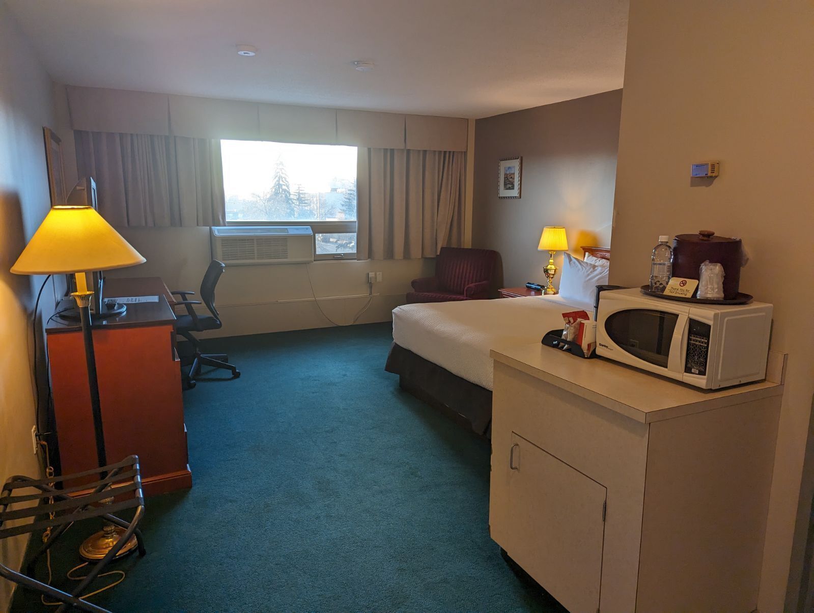 Ein Hotelzimmer mit Bett, Schreibtisch, Stuhl, Lampe und einer Mikrowelle.