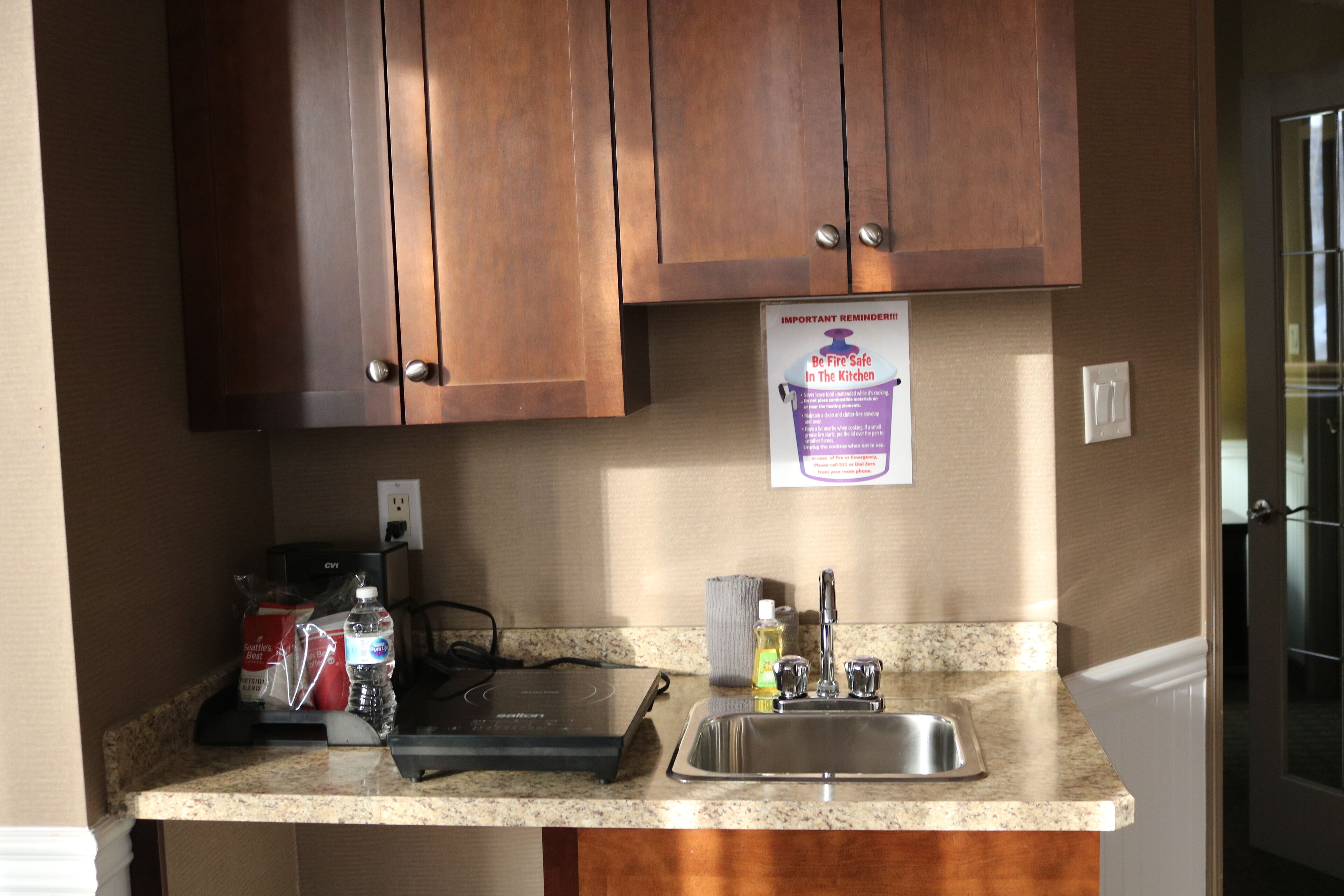 A kitchen with wooden cabinets, a granite countertop, a built-in electric stove, a sink, and a fire safety reminder sign.