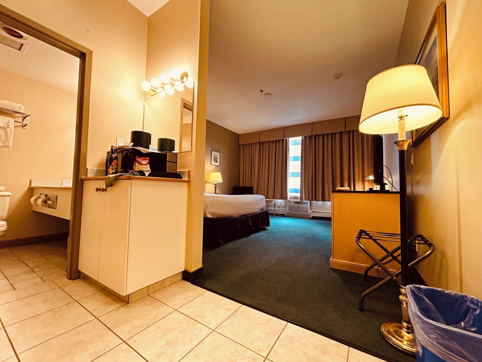 Een hotelkamer met een bed, een bureau met lamp, een prullenbak en een badkamer met toilet en wastafel.