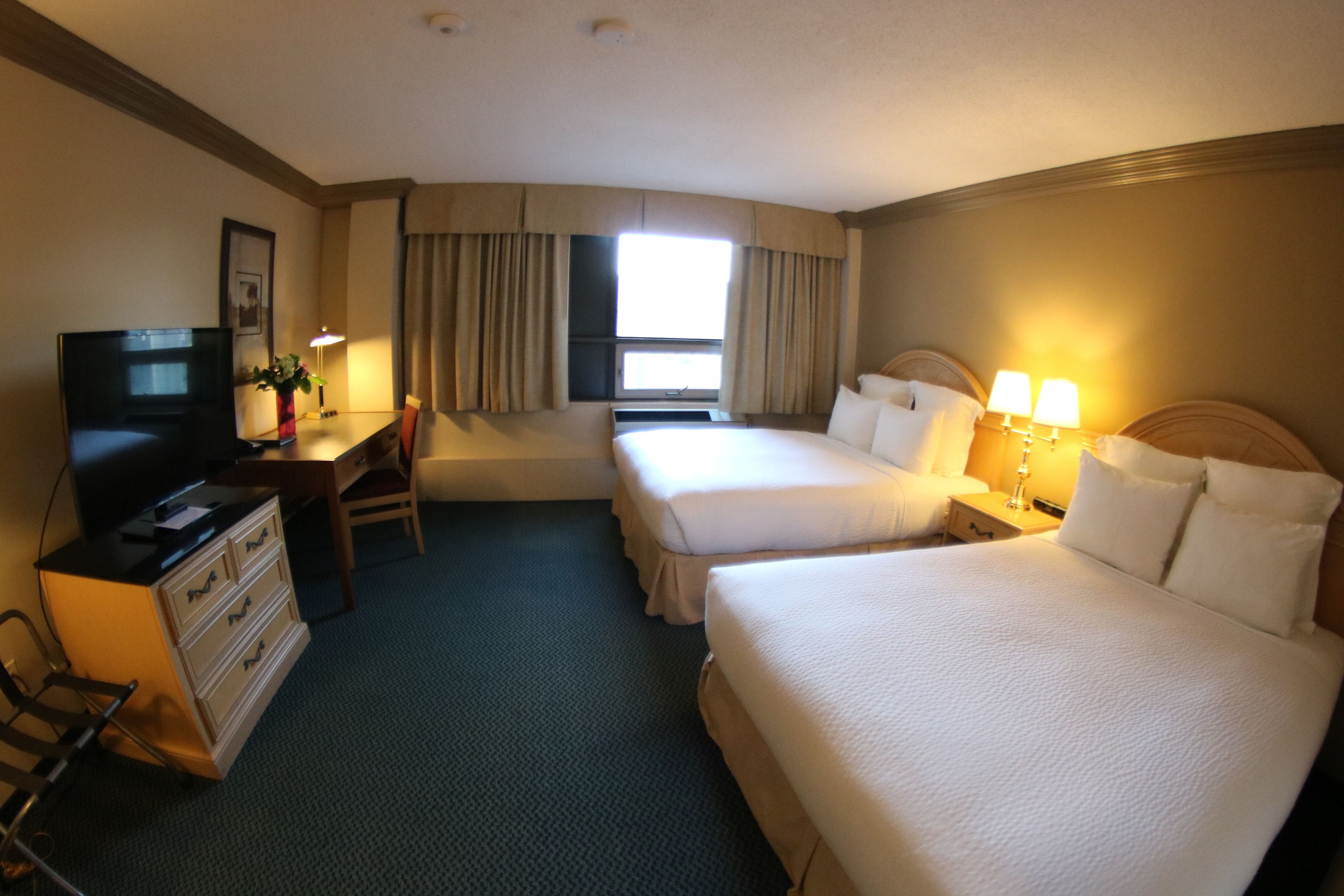 Une chambre d’hôtel avec deux lits, un bureau avec une chaise, une commode, une télévision et une fenêtre avec des rideaux.