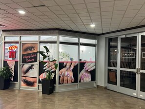 A salon with a 'Happy Nail Corner' sign, a neon 'OPEN' sign, and a 'THE KEG Steakhouse-Bar' sign. - Nomad Hotel and Suites (Fort McMurray)