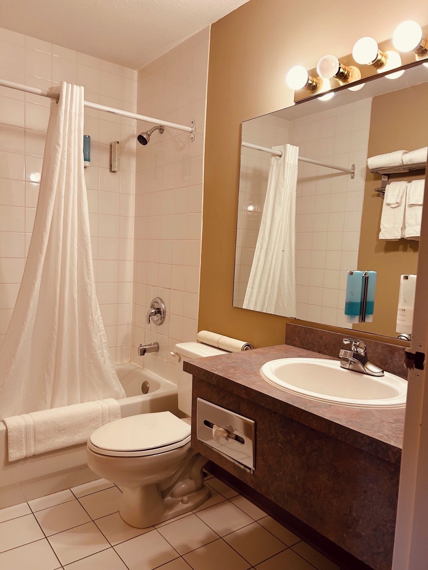 A bathroom with a bathtub, toilet, sink, and a mirror with lights.