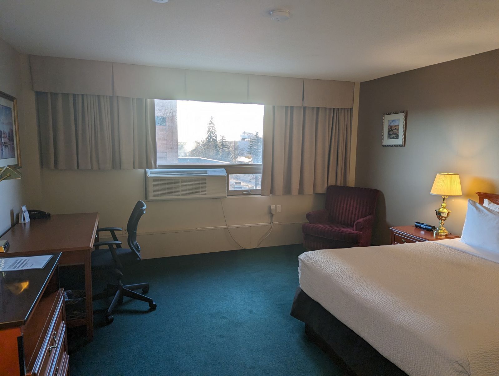 Habitación de hotel con cama, escritorio, silla y aire acondicionado.