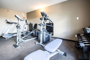 A gym with exercise equipment including a treadmill, elliptical, and weight bench. - Nomad Hotel and Suites (Fort McMurray)